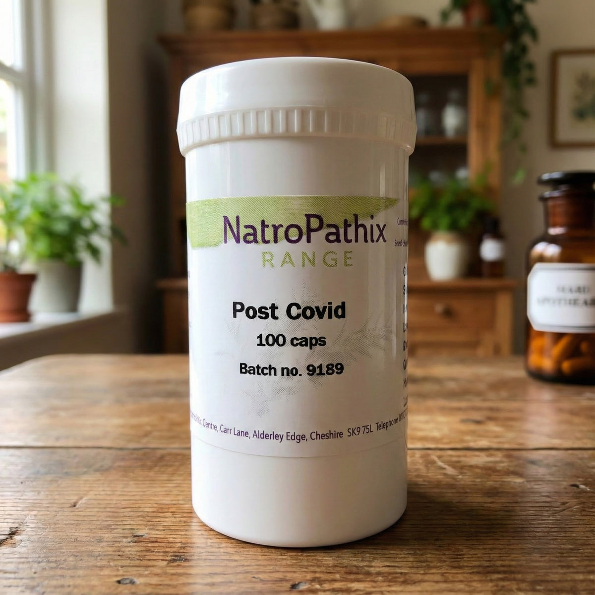 A white bottle labeled "Post Covid - 100 Caps" sits on a wooden table in a bright kitchen, highlighting its adaptogenic capsules formulated to support recovery after COVID.