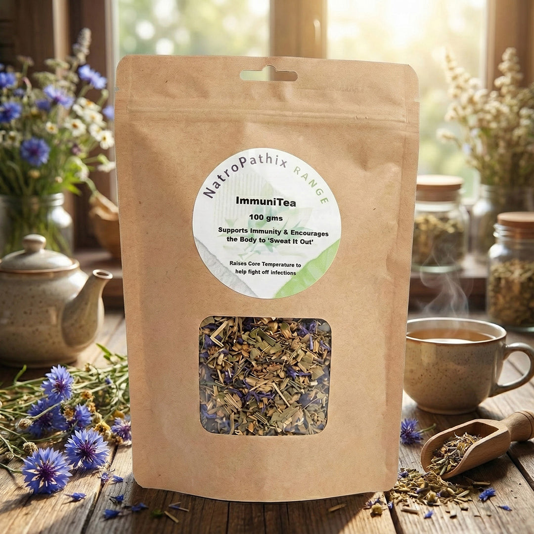 A 100gms bag of ImmuniTea rests on a table beside a teapot, cup, and flowers, providing immune system support with each soothing sip.