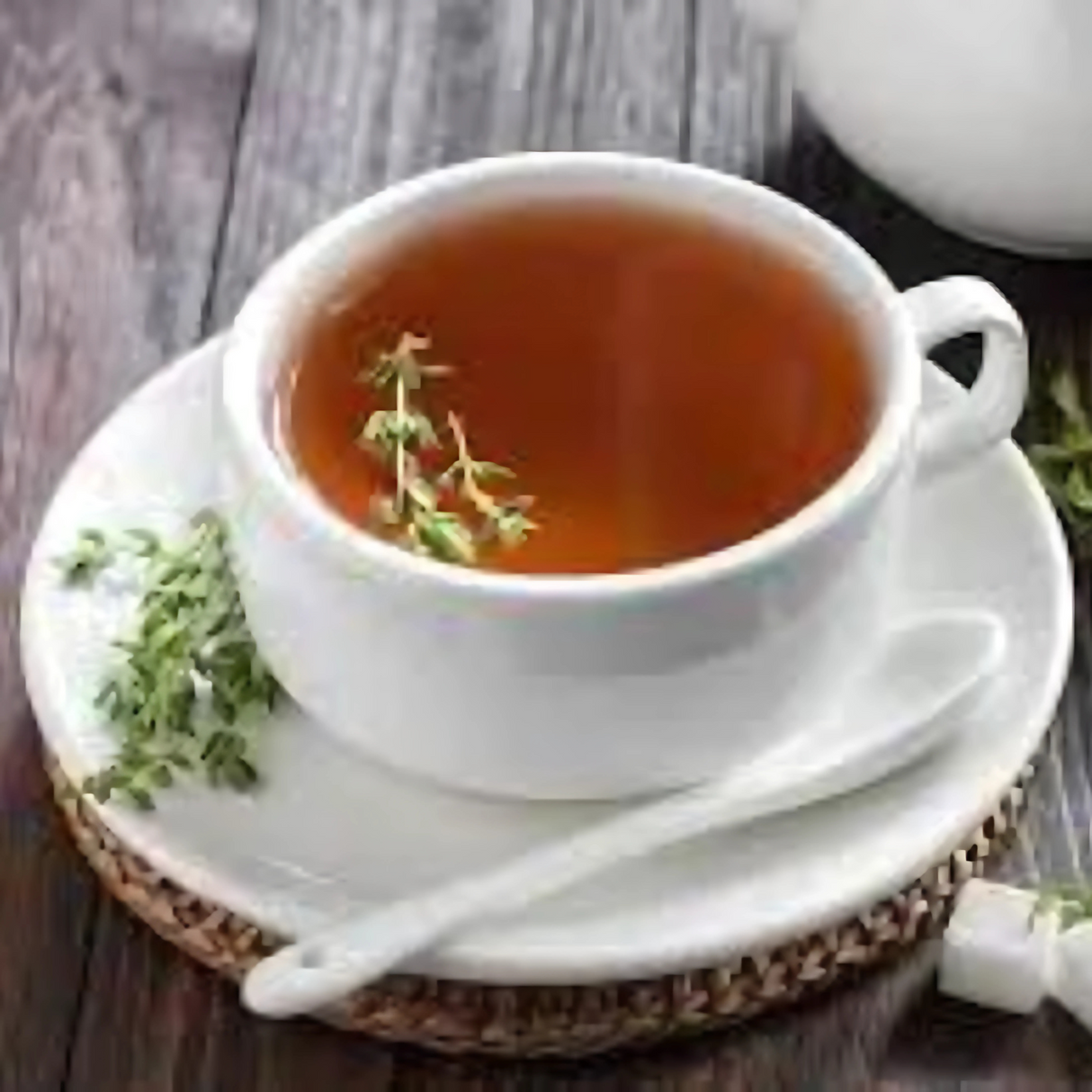 A cup of Uterine Tea - 100gms for women’s wellness, garnished with thyme, rests on a saucer with a spoon on a wooden table.