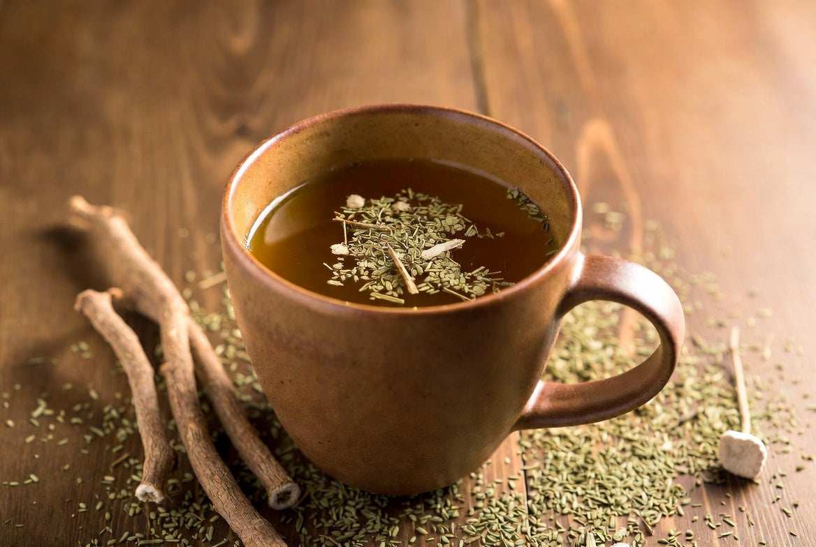 Ceramic mug filled with golden herbal tea for gut lining repair, surrounded by healing herbs on wooden table