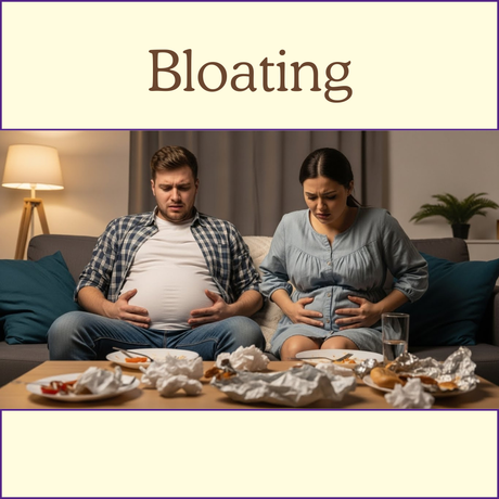 Man and woman on couch holding their stomachs, looking uncomfortable, with food and wrappers on table.