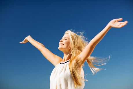 Smiling woman with arms raised, standing outdoors under a clear blue sky.