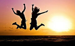 Two people jumping in the air on a beach at sunset, silhouetted against the colorful sky.
