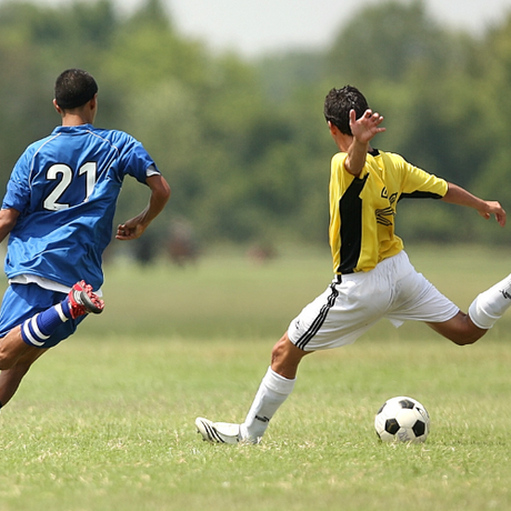 Two soccer players compete for the ball on a grassy field, one in blue and the other in yellow.