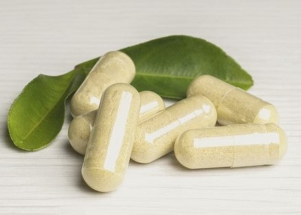 Several beige capsules are placed on a white surface with two green leaves in the background.