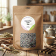 A brown packet of Liquorice Root - Tincture, Herbal Tea or Powder rests on a table with loose tea, teapot, cup, and licorice sticks—ideal for those seeking natural support for acid reflux or heartburn.