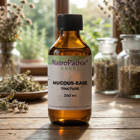 A brown bottle labeled "Mucous-Ease Tincture - 200/300ml" sits on a wooden table with herbs, an herbal tincture designed to help ease congestion and naturally support clear airways.