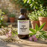 A bottle of Vitex and Centaury Tincture - 200/300ml sits on a wooden table with herbs and potted plants, specially formulated to support hormonal balance and provide relief from menopausal symptoms.