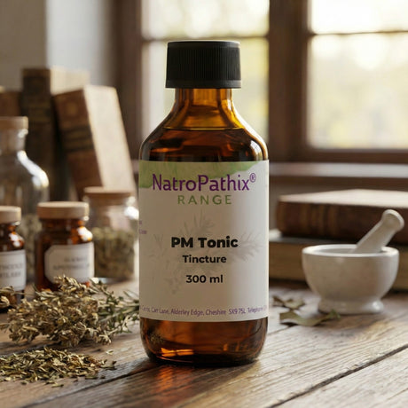 A brown bottle labeled "PMTonic - 200/300ml" rests on a wooden table beside herbs and books, indicating its role as a uterine tonic for menstrual cycle support.