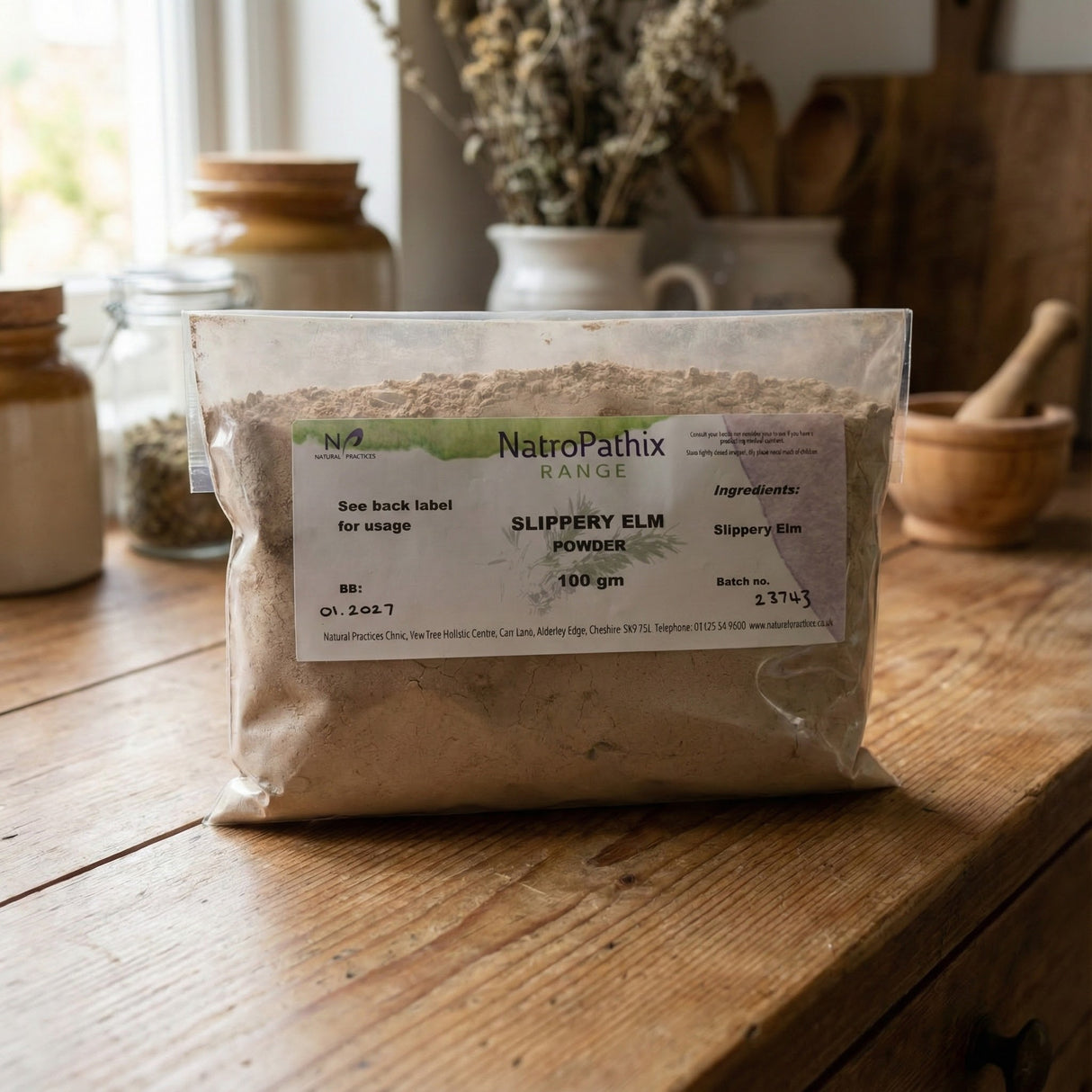 A clear bag of Slippery Elm Powder - 100 gms rests on a wooden table with jars behind it, emphasizing its natural detox properties that promote digestive health.