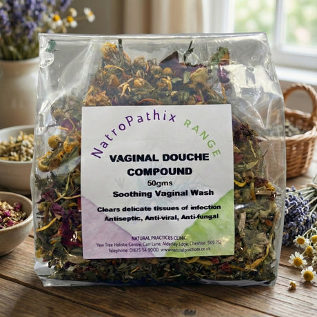 A 50g bag of Vaginal Douche Compound sits on a wooden table, valued for its anti-bacterial properties, with blurred plants in the background.