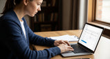Woman using a laptop at a desk with a window in the background