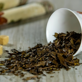 Loose herbal tea leaves from a white cup spill onto the table beside sugar cubes—perfect for brewing SleepiTime Tea (50 & 100gms) to promote restorative, calming sleep.